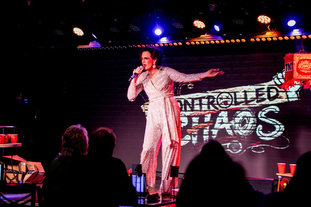 Singer in a sequin jumpsuit in front of the Controlled Chaos logo